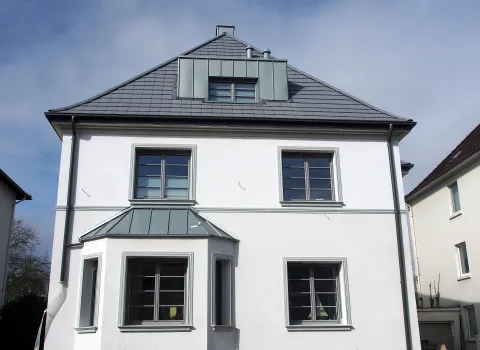 Ein modernisierter Altbau mit klaren Linien, neuer Fensterverglasung und einem grauen Satteldach. Die frisch renovierte Fassade wirkt gepflegt und stilvoll.