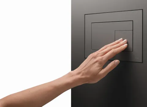 Eine Person drückt die kleine Spültaste auf einer anthrazitfarbenen TECEvelvet WC-Betätigungsplatte.