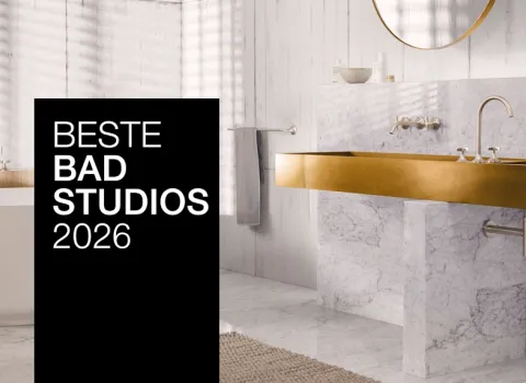 Ein stilvolles Bad mit goldenen Armaturen, Marmorwaschtisch und freistehender Badewanne. Ein schwarzer Banner mit "Beste Badstudios 2026" ist prominent im Bild.