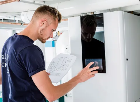Ein SHK-Anlagenmechaniker mit Datenblatt stellt eine Heizungsanlage ein.