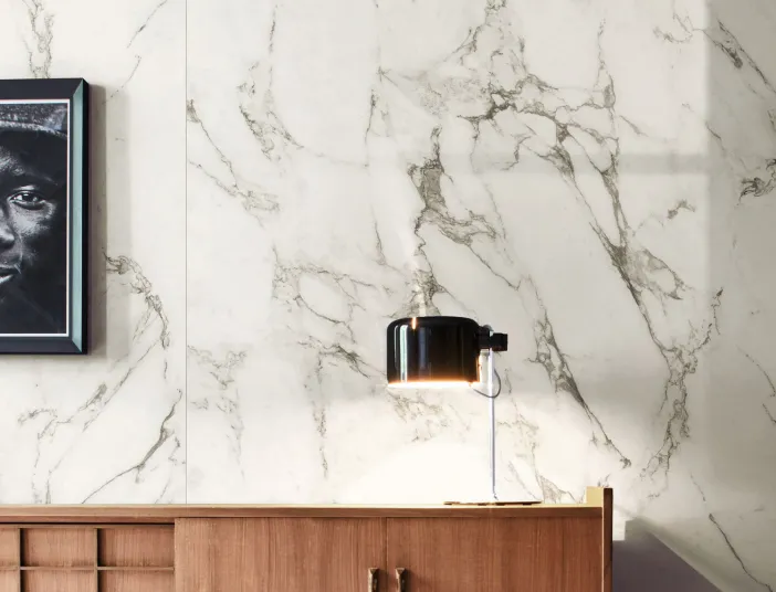 Holz-Sideboard mit Nachttisch-Lampe vor Wand mit Fliesen in Marmoroptik von Marazzi.